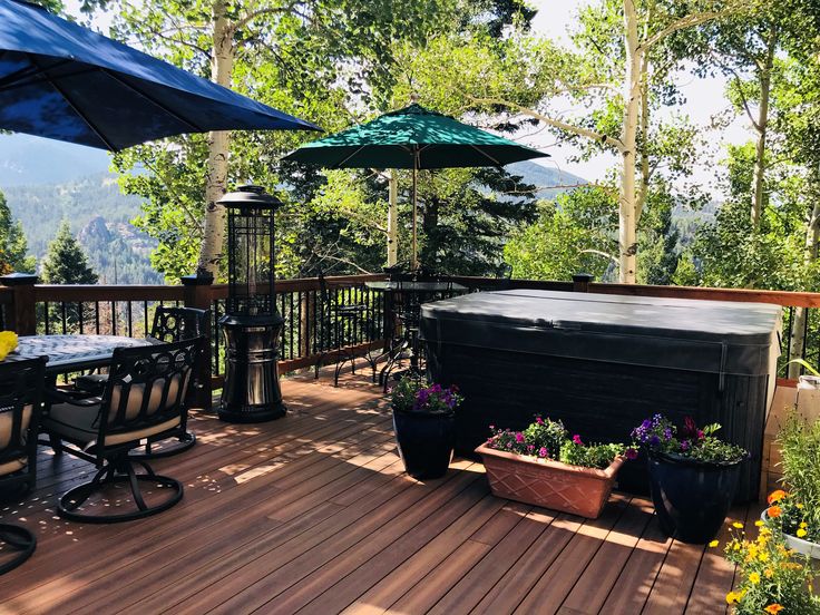 a hot tub sitting on top of a wooden deck next to flowers and an umbrella