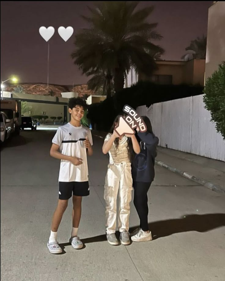 two people standing next to each other in front of a building at night with heart shaped balloons