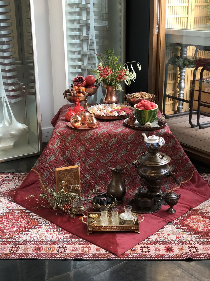 the table is covered with various foods and dishes on top of an ornate red cloth