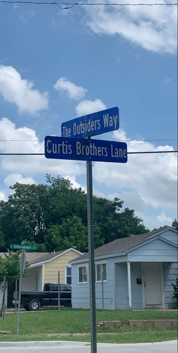 two blue street signs sitting on the side of a road in front of some houses