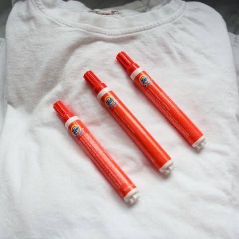 three orange pens sitting on top of a white t - shirt next to each other