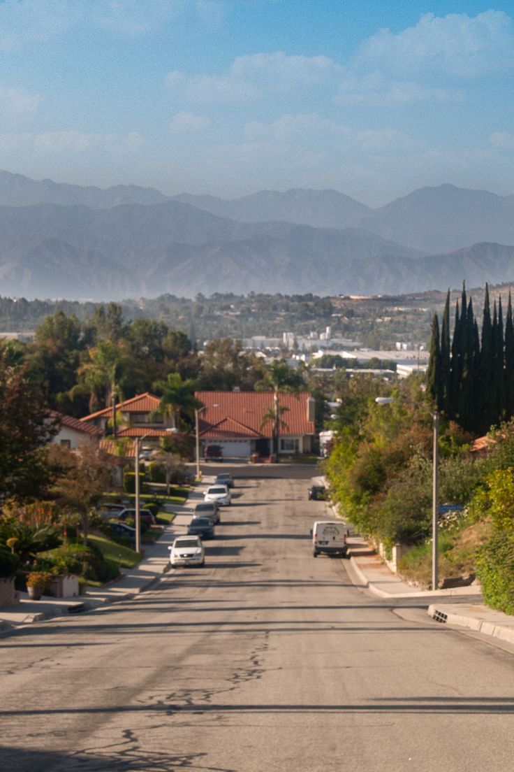 an empty street with cars parked on both sides and mountains in the distance behind it