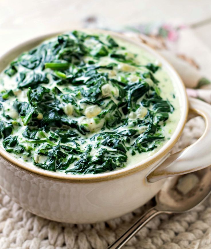 a bowl filled with spinach and cheese on top of a knitted place mat