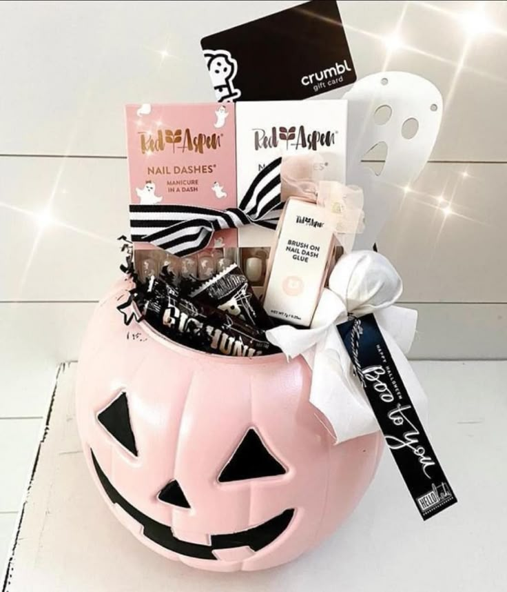 a pink pumpkin shaped basket filled with candy and treats next to a white mask on the wall