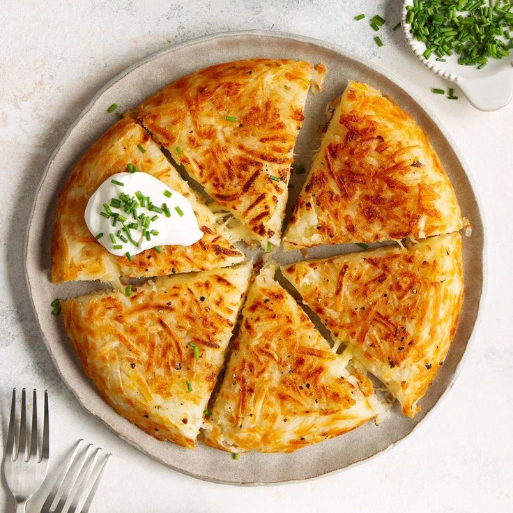 a pizza with cheese and herbs on a plate next to a fork, knife and napkin