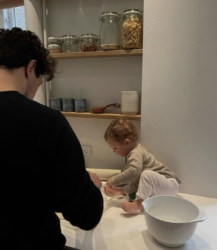 a man standing next to a baby on top of a kitchen counter in front of a bowl