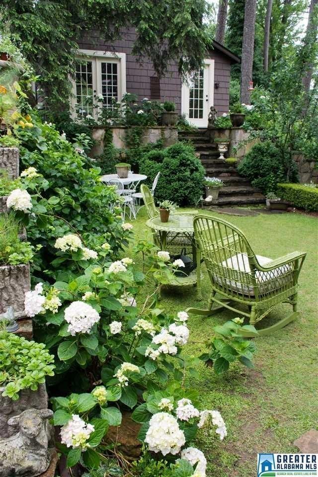 a green chair sitting on top of a lush green field next to flowers and bushes