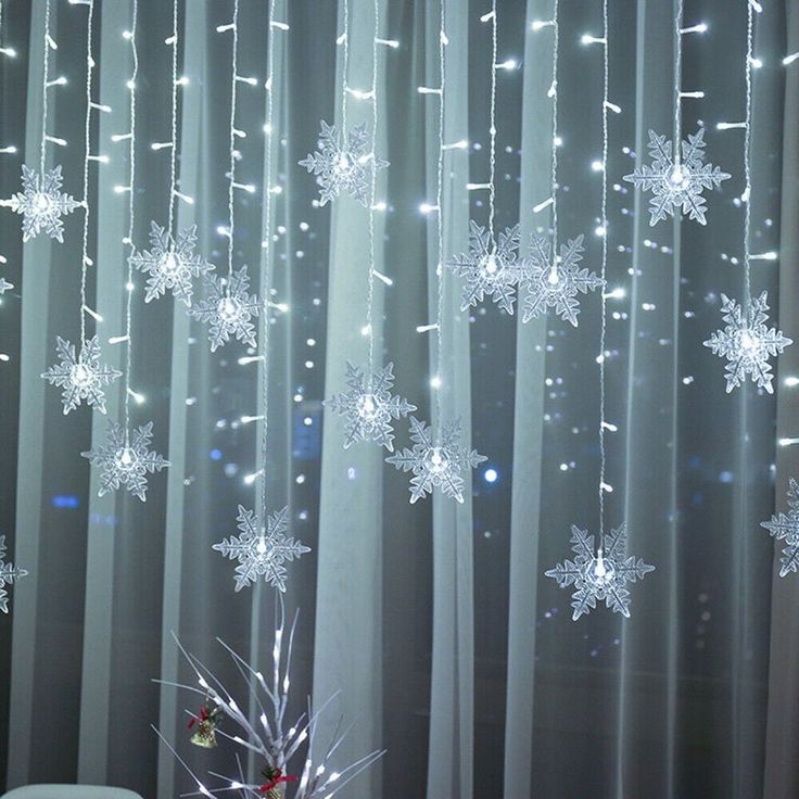 snowflakes are hanging from the sheer curtains in front of a christmas tree with lights