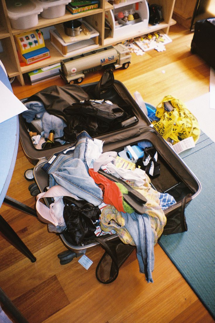 an open suitcase filled with clothes on top of a wooden floor next to a book shelf