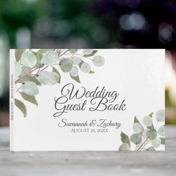 a wedding guest book sitting on top of a wooden table with greenery in the background