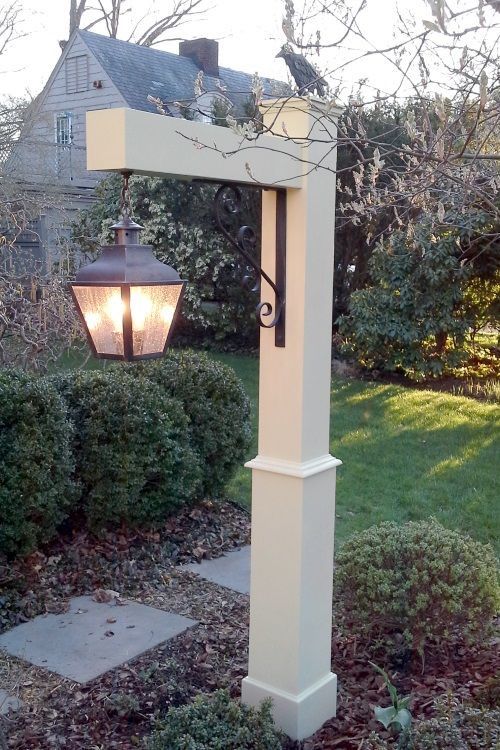 a light that is on top of a post in the grass near bushes and trees