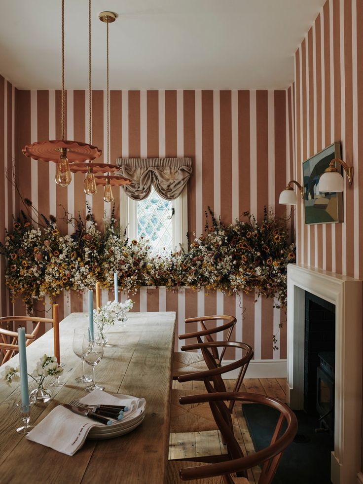 a dining room with striped wallpaper and wooden table surrounded by candles, flowers and greenery