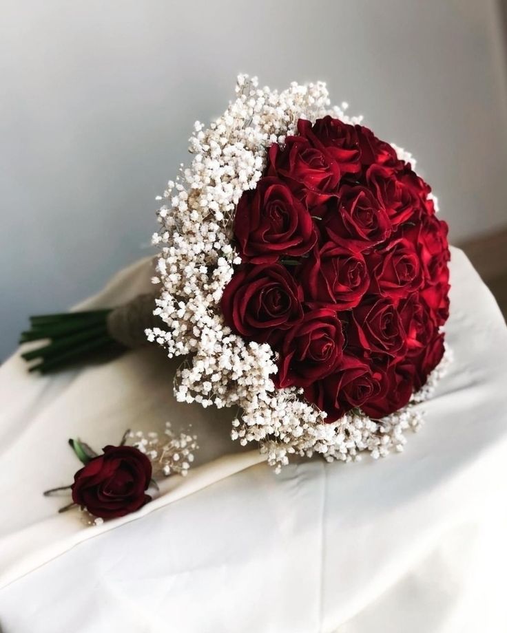 a bouquet of red roses and baby's breath on a white cloth with pearls