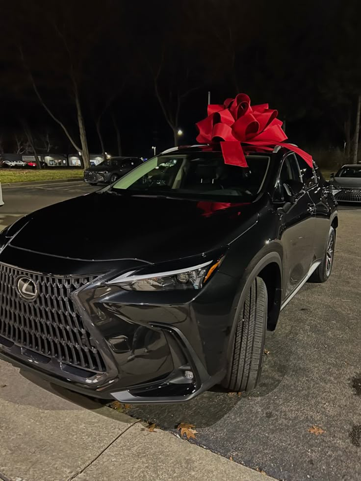 a black car with a red bow on the hood is parked in a parking lot