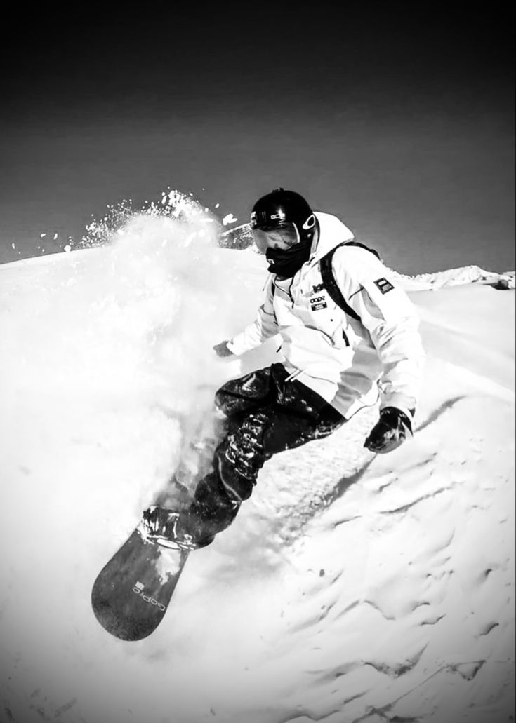 a man riding a snowboard down the side of a snow covered slope in black and white