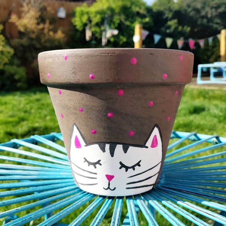 a pot with a cat face painted on it sitting on a table in the grass