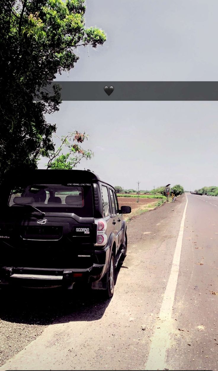 a black truck parked on the side of a road next to a tree and grass covered field