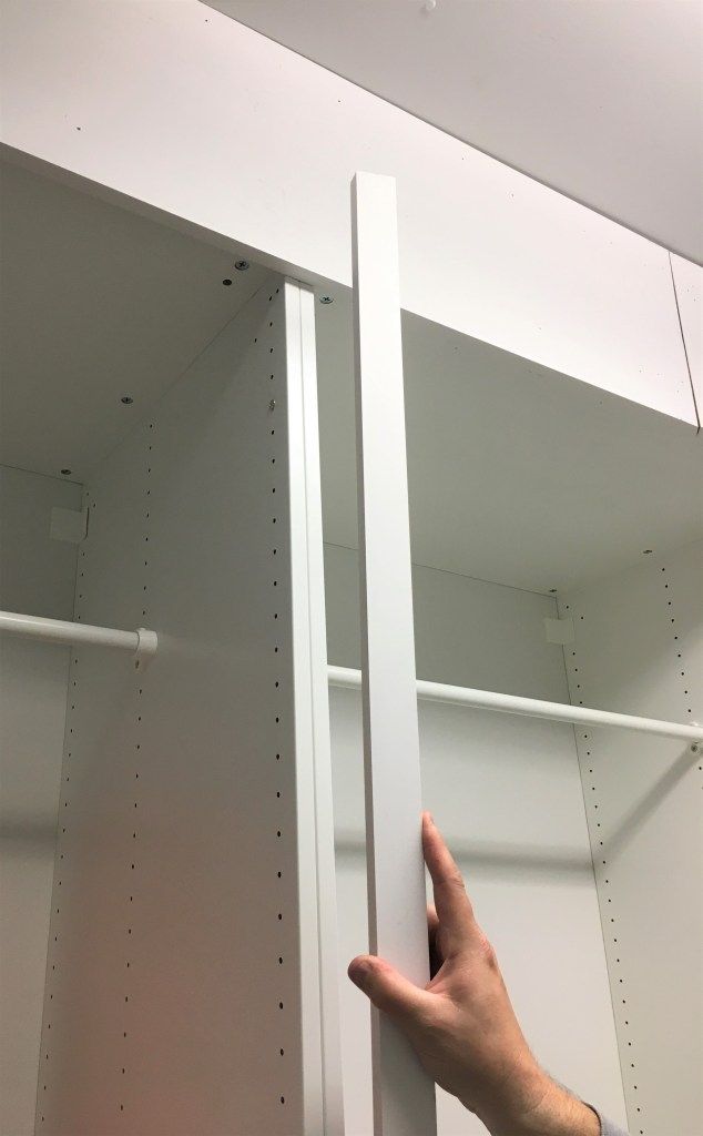 a person's hand pointing at the bottom of a white shelving unit in a store