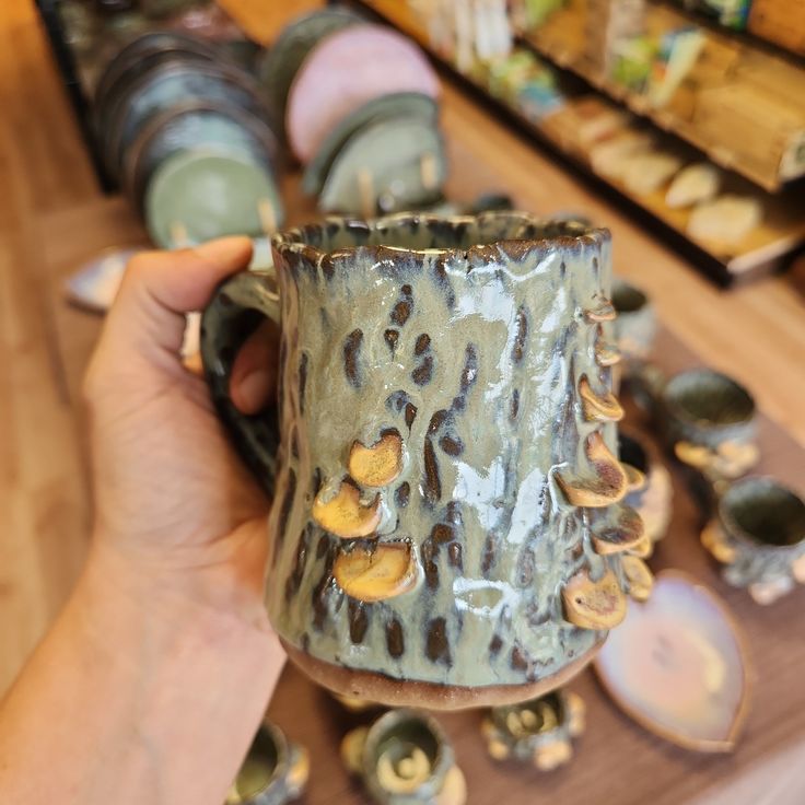 a person holding a coffee mug in front of some cups on a table with other items