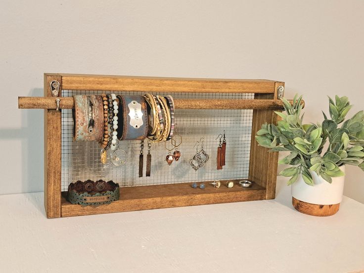 a wooden shelf with bracelets and earrings on it next to a potted plant