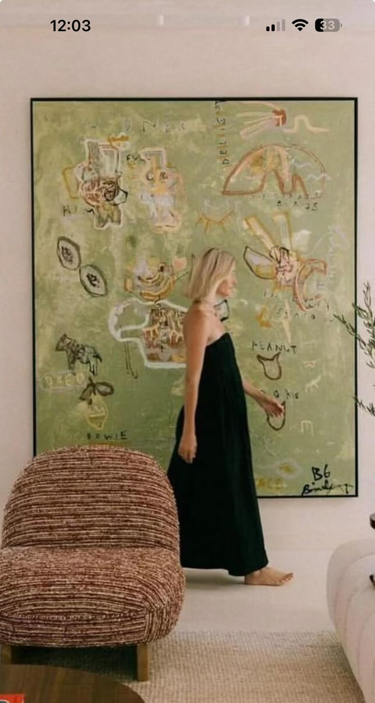 a woman standing in front of a painting on the wall next to a chair and ottoman