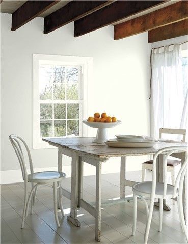 a dining room with yellow painted walls and white chairs, an oval table surrounded by fruit