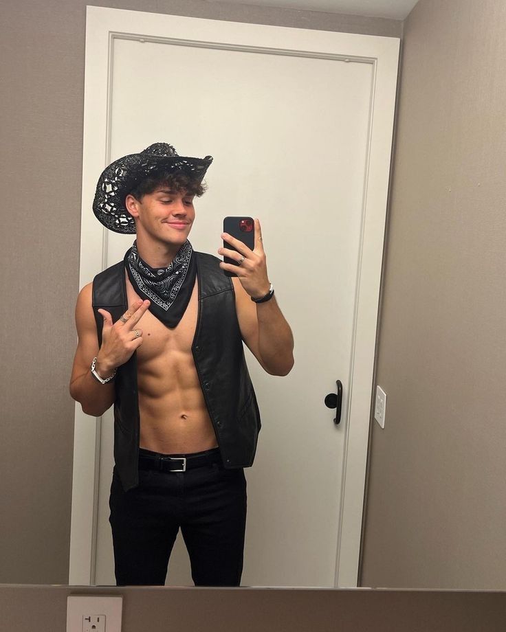 a shirtless man taking a selfie in front of a mirror wearing a cowboy hat