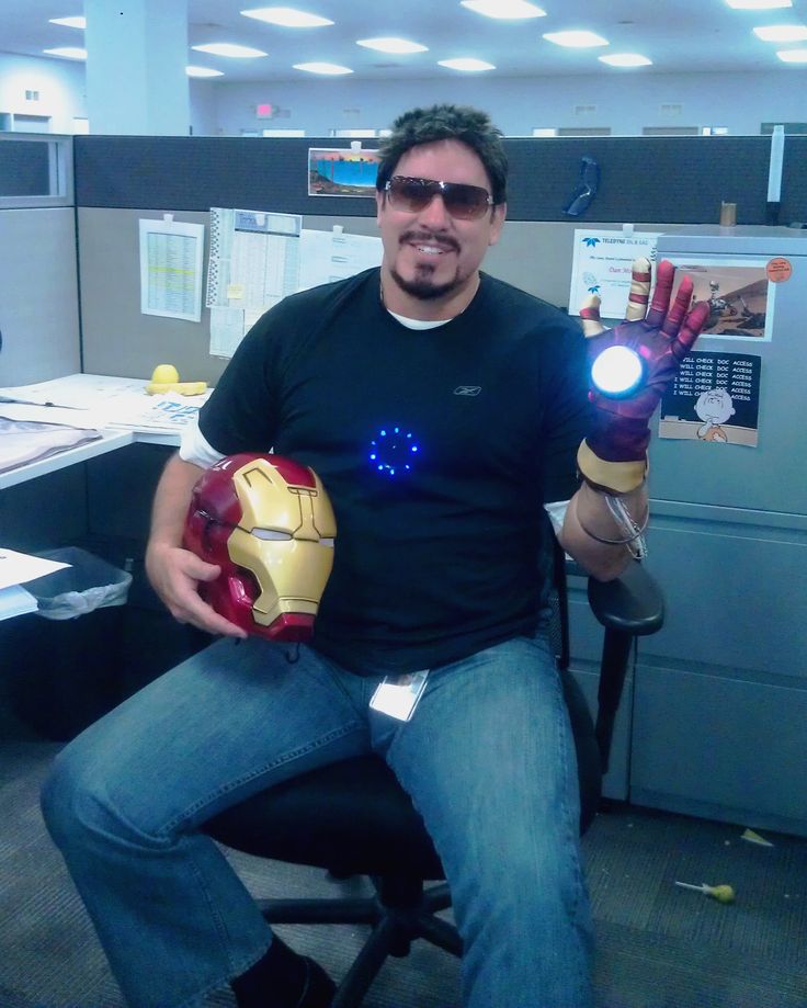 a man sitting in an office chair holding up two iron - man gloves with glowing eyes