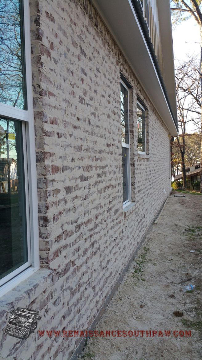 the side of a brick house that has been painted white and is next to a tree