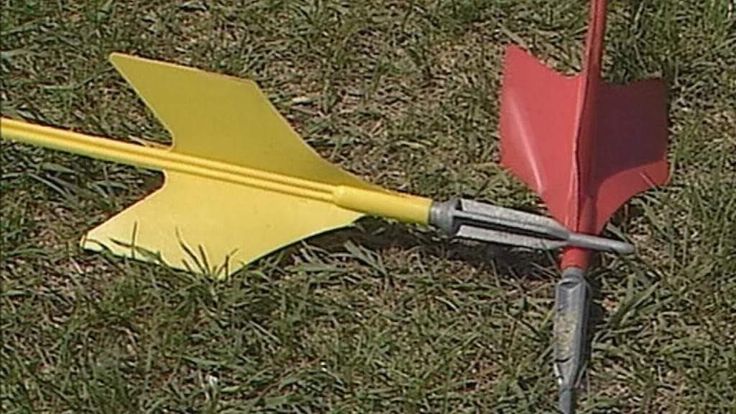 a red and yellow arrow laying on top of green grass next to a tool in the ground