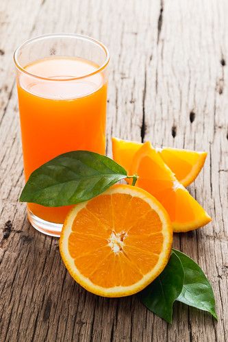 orange juice in a glass next to sliced oranges and leaves on a wooden table