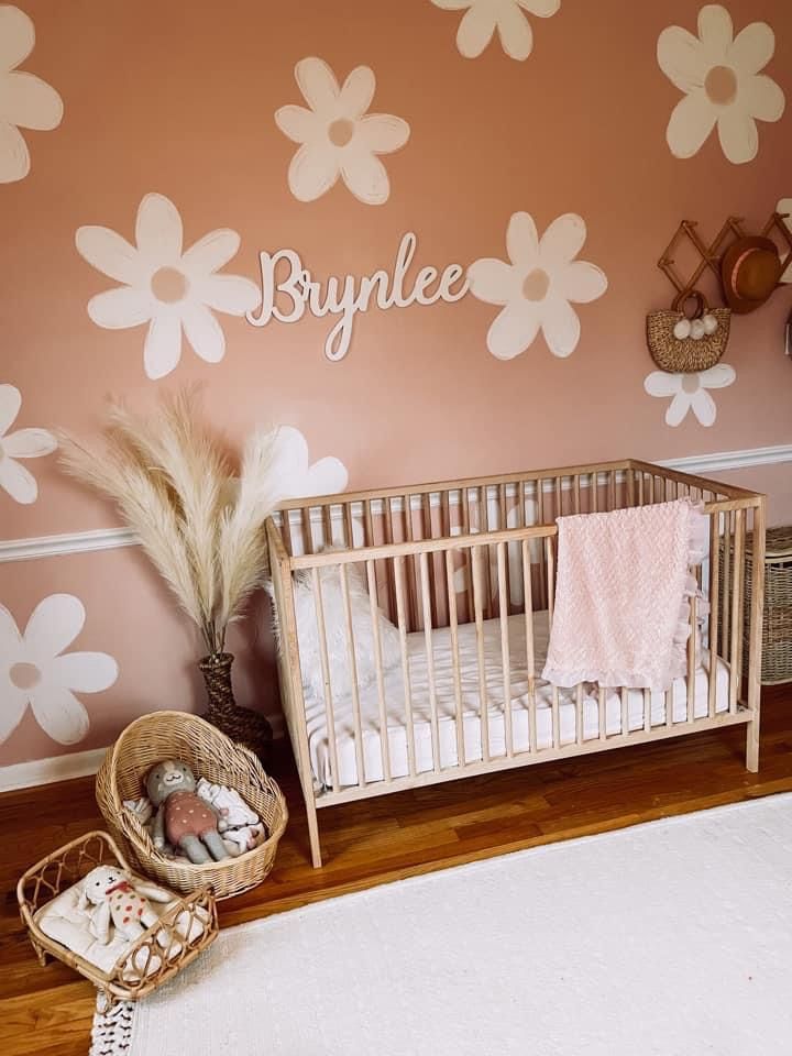 a baby's room with pink and white flowers painted on the wall, along with a crib