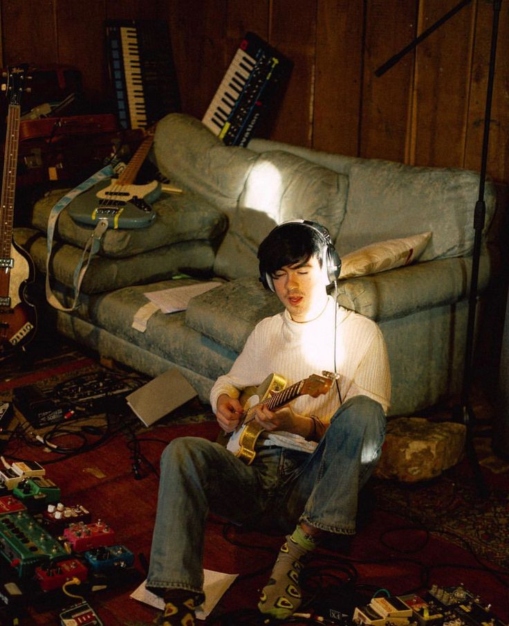 a young man sitting on the floor with headphones in his ears while playing an instrument