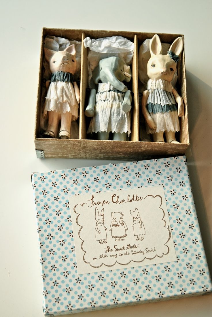 three little figurines in a wooden box on a white table with a blue and white checkered napkin