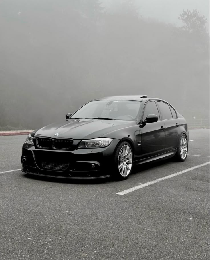 a black car parked in a parking lot on a foggy day