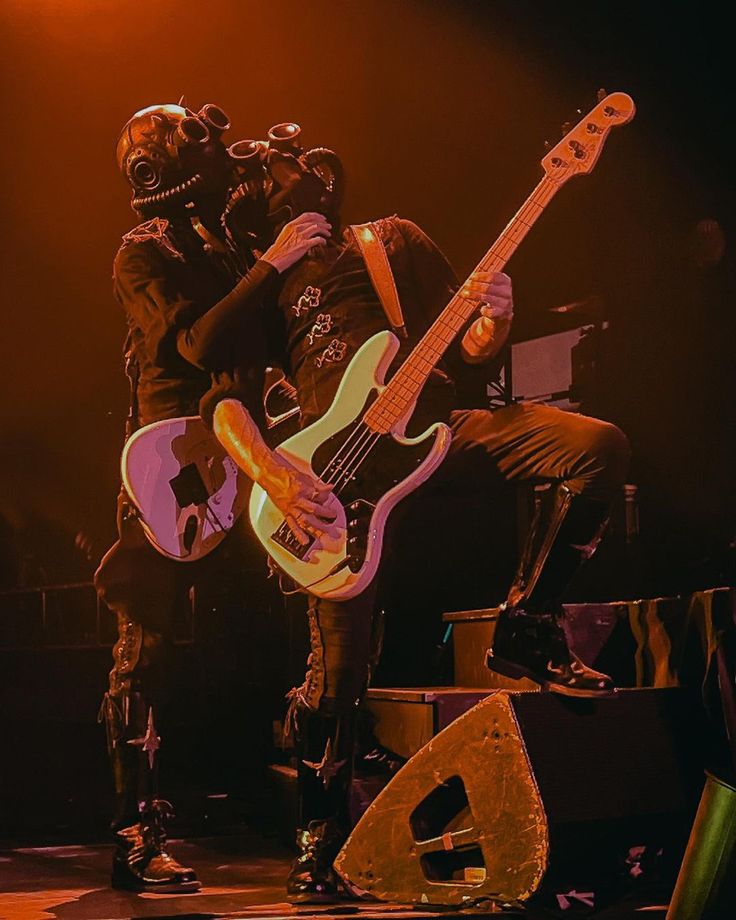 two men with masks on their faces are playing guitars and singing into microphones at a concert