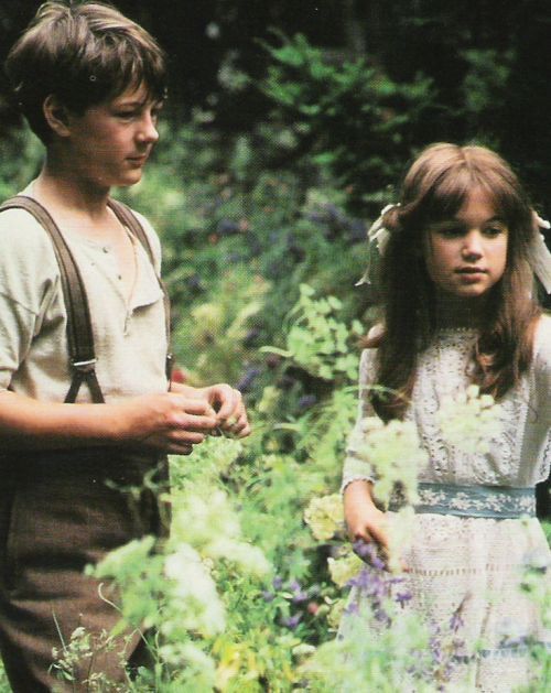 a young boy and girl are standing in the tall grass, looking at each other