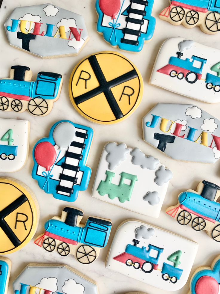 decorated cookies with trains and balloons are displayed on a white tablecloth, top view