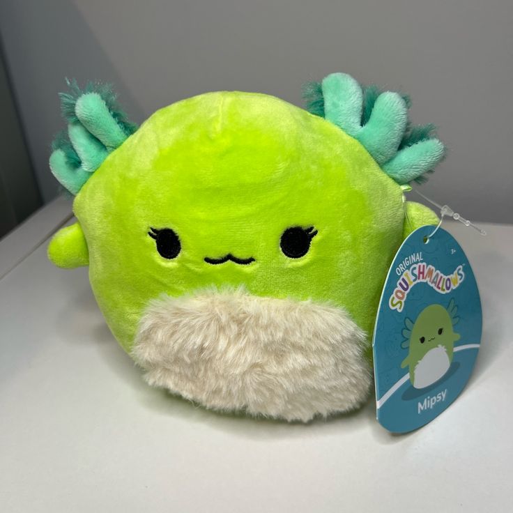 a green stuffed animal sitting on top of a white table next to a blue tag