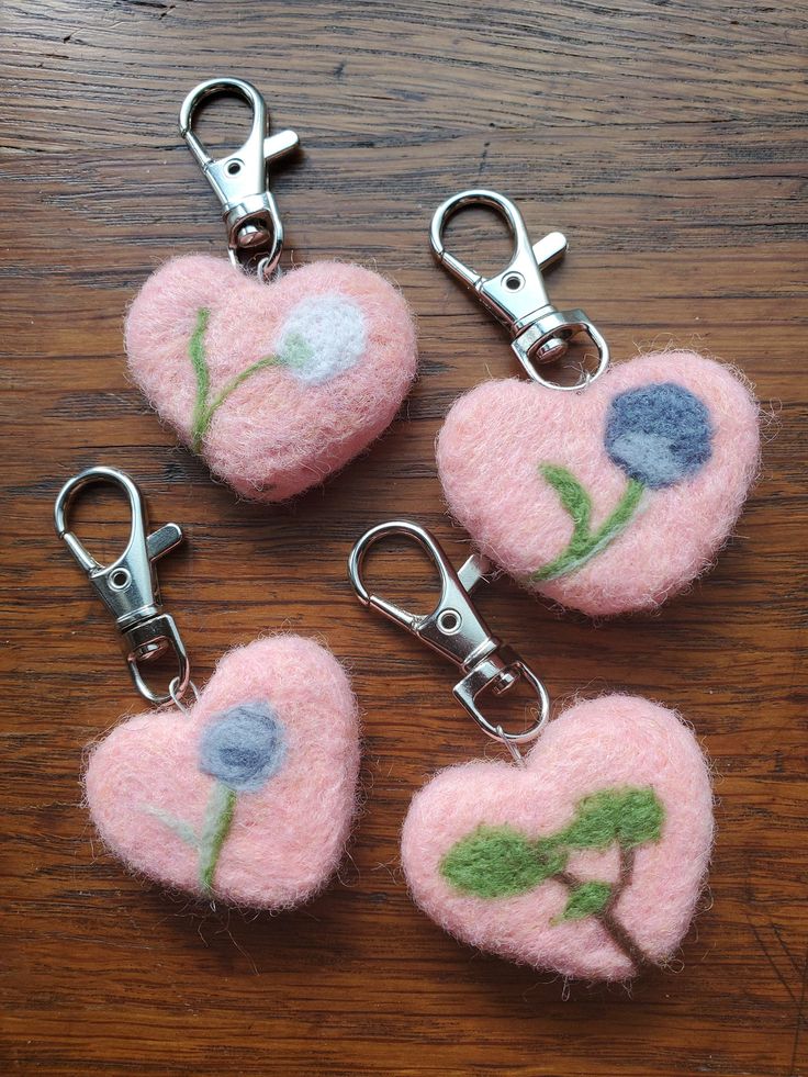 four pink heart shaped key chains with blue flowers on them sitting on a wooden table