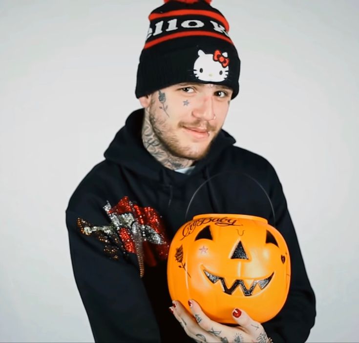 a man in a hello kitty hat holding a jack - o'- lantern