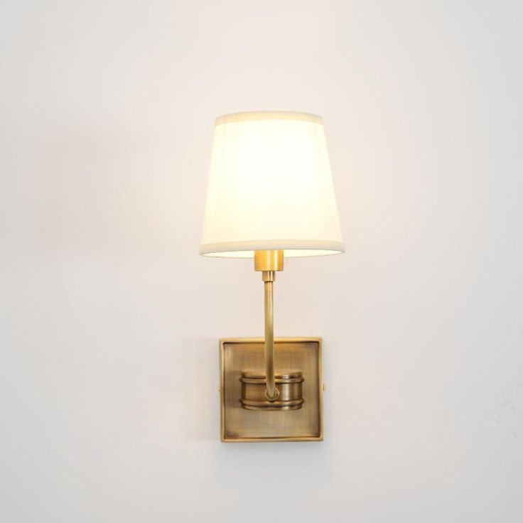 a wall light with a white shade on it's side and a gold finish