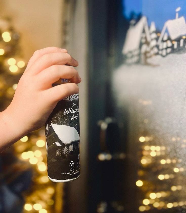 a hand holding a can of water in front of a christmas tree