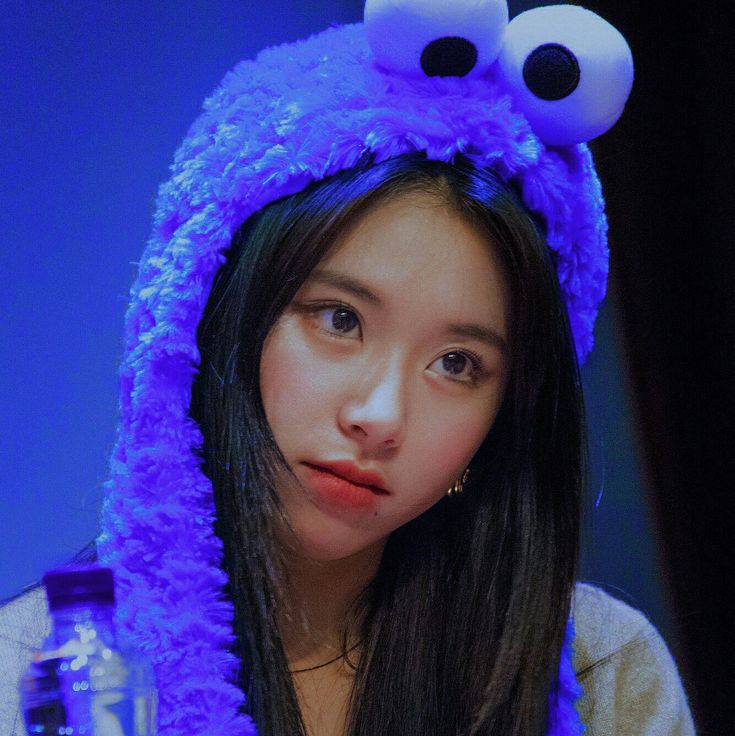 a young woman wearing a purple furry hat with eyes on it's head and holding a water bottle in front of her face