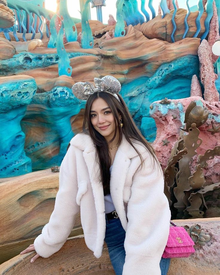 a woman sitting on top of a wooden barrel in front of a fake waterfall wall