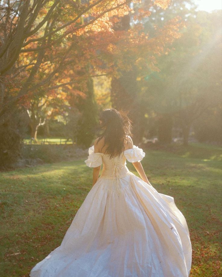 a woman in a white dress is walking through the grass with her back to the camera