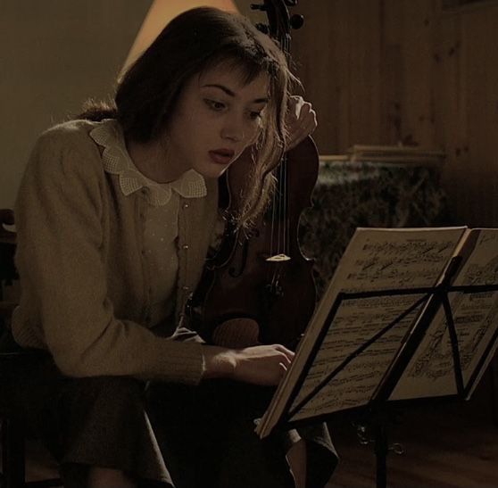 a woman sitting in front of a musical instrument on top of a wooden floor next to a lamp