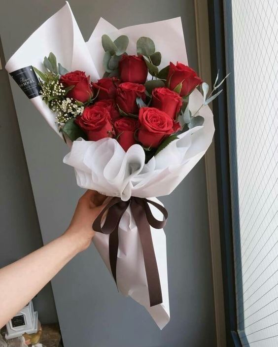 a person holding a bouquet of red roses in their left hand and the flowers are wrapped in white paper