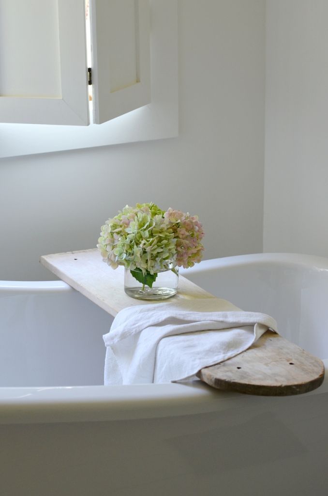 a white bath tub sitting under a window next to a vase with flowers in it