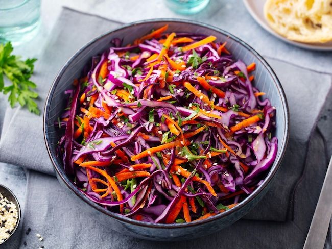 a bowl filled with red cabbage and carrots on top of a table next to bread